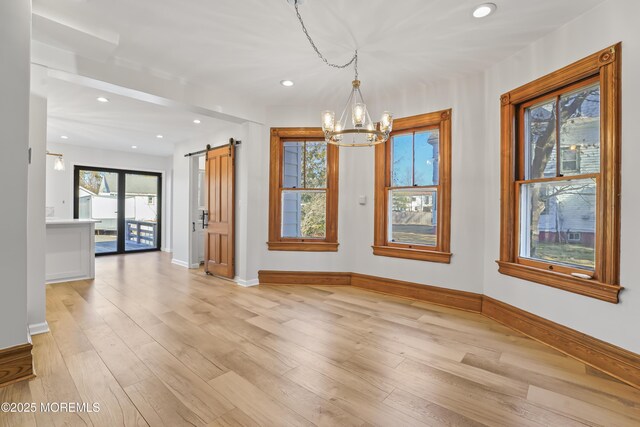 unfurnished dining area with light hardwood / wood-style flooring, a barn door, and a chandelier