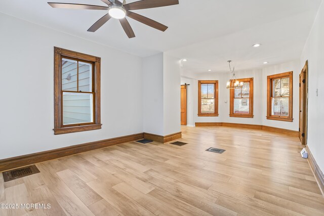 spare room with ceiling fan with notable chandelier and light wood-type flooring