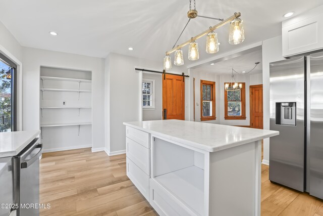 kitchen with stainless steel appliances, light hardwood / wood-style floors, white cabinets, a kitchen island, and a barn door