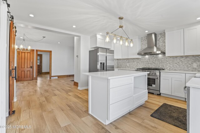 kitchen with a kitchen island, appliances with stainless steel finishes, decorative light fixtures, white cabinetry, and wall chimney range hood