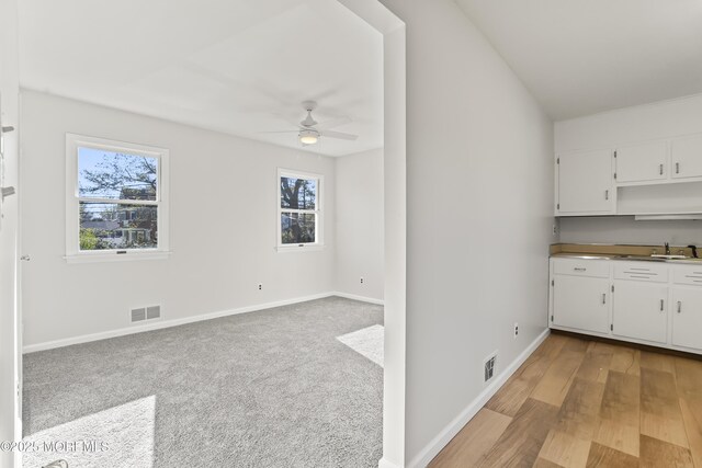 kitchen featuring ceiling fan, light colored carpet, sink, and white cabinets