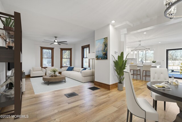 living room featuring ceiling fan with notable chandelier and light wood-type flooring