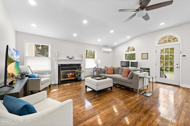 living room featuring dark wood-type flooring, vaulted ceiling, an AC wall unit, ceiling fan, and a fireplace