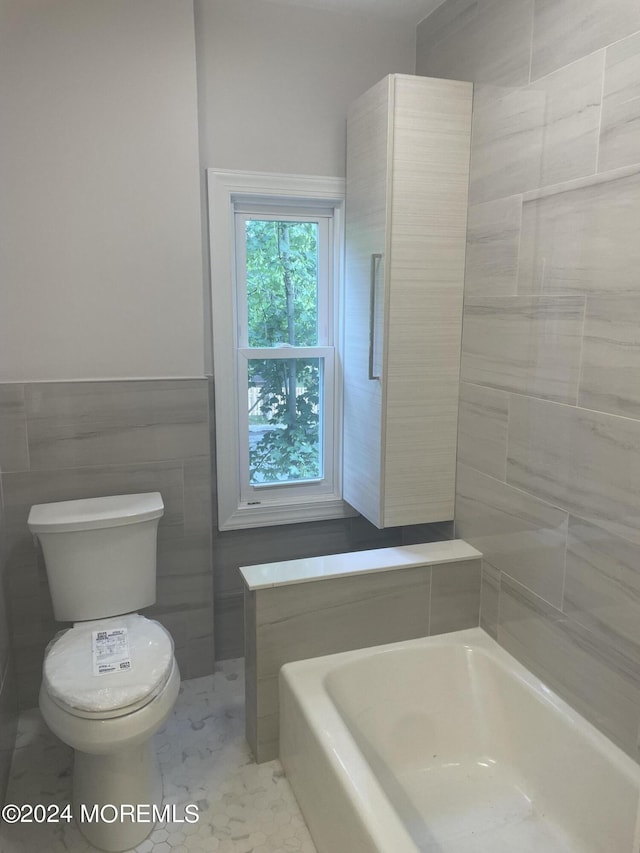 bathroom featuring toilet, a bathing tub, and tile walls