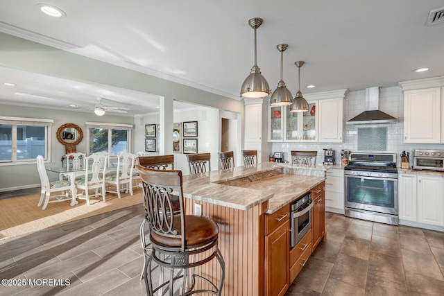 kitchen featuring appliances with stainless steel finishes, white cabinetry, a center island, light stone countertops, and wall chimney exhaust hood