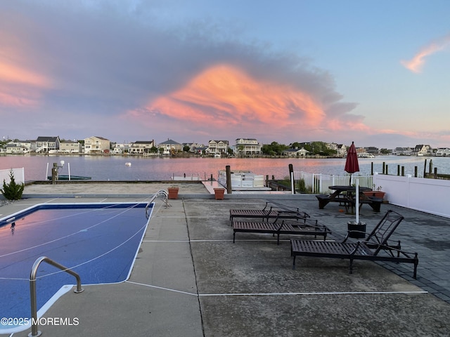 pool at dusk featuring tennis court and a water view