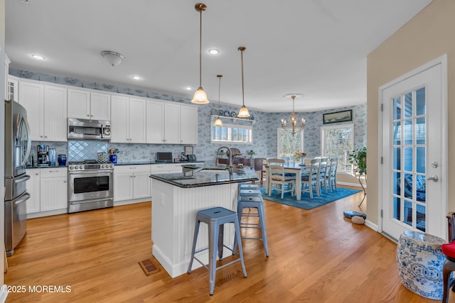 kitchen with white cabinetry, stainless steel appliances, light hardwood / wood-style floors, an island with sink, and decorative light fixtures