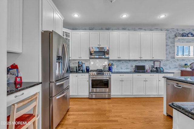 kitchen with white cabinetry, dark stone counters, stainless steel appliances, light hardwood / wood-style floors, and decorative backsplash