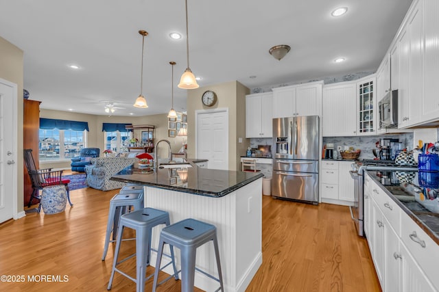 kitchen featuring hanging light fixtures, appliances with stainless steel finishes, a kitchen breakfast bar, a kitchen island with sink, and white cabinets