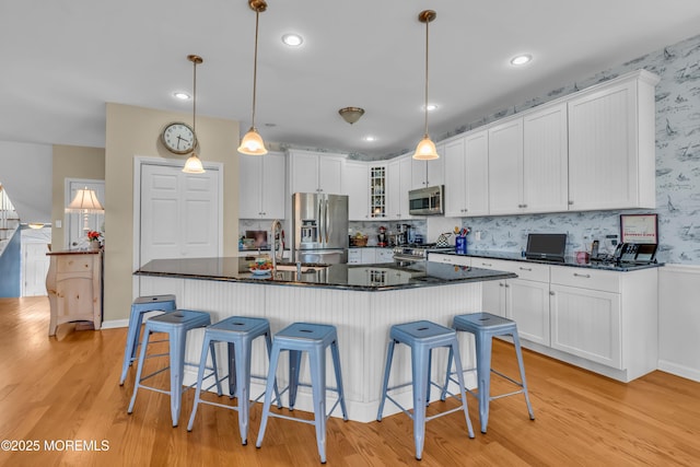 kitchen with pendant lighting, stainless steel appliances, a kitchen island with sink, and white cabinets