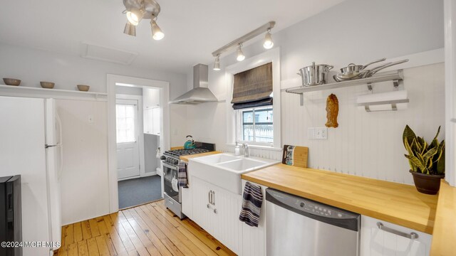 kitchen with wood counters, sink, wall chimney range hood, stainless steel appliances, and white cabinets