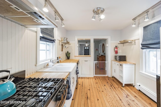 kitchen featuring wood counters, range hood, white cabinetry, baseboard heating, and stainless steel appliances