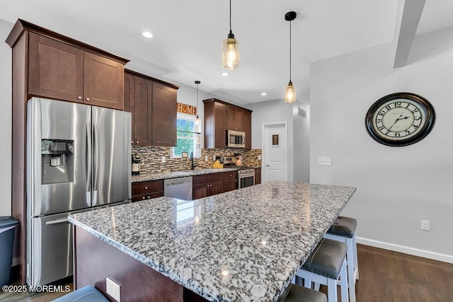 kitchen featuring stainless steel appliances, light stone countertops, a center island, and pendant lighting