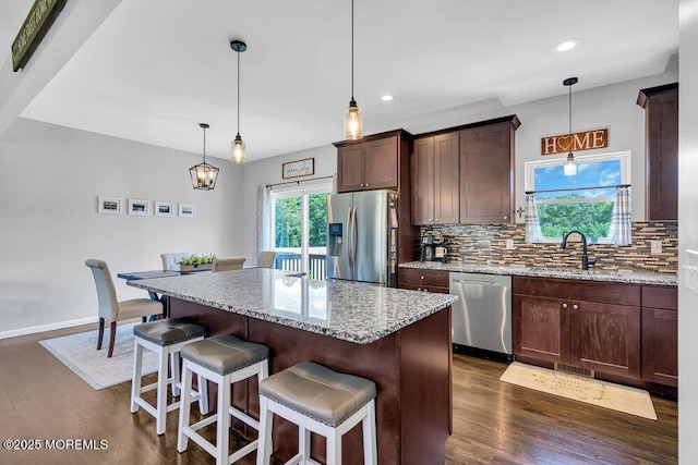 kitchen with appliances with stainless steel finishes, light stone countertops, sink, and a kitchen island