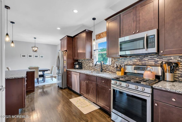 kitchen with light stone counters, hanging light fixtures, stainless steel appliances, and sink