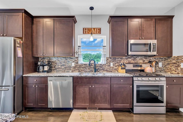 kitchen with sink, backsplash, stainless steel appliances, light stone counters, and decorative light fixtures