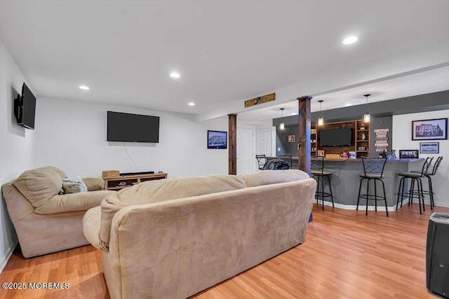 living room featuring decorative columns, light hardwood / wood-style floors, and indoor bar