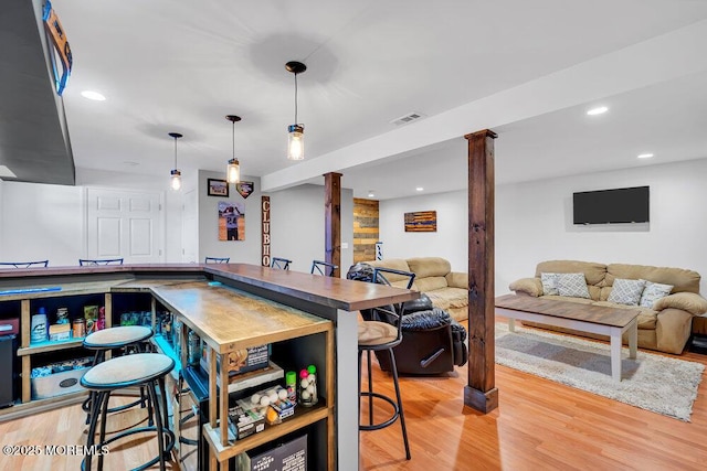 bar featuring hanging light fixtures, decorative columns, and light hardwood / wood-style flooring