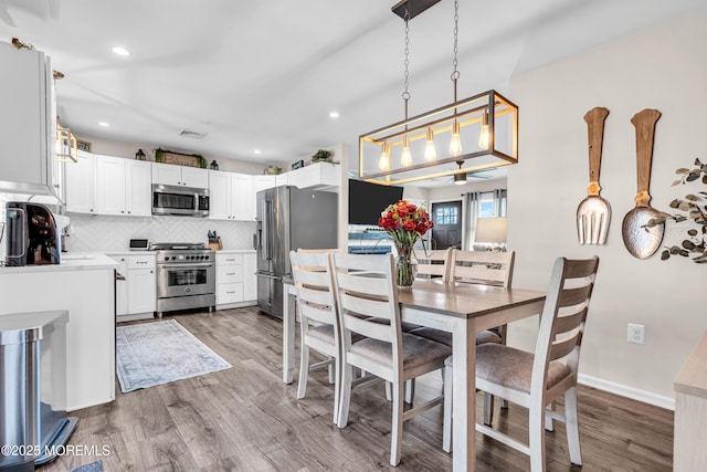 kitchen featuring hardwood / wood-style floors, pendant lighting, backsplash, white cabinets, and premium appliances