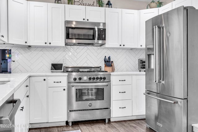 kitchen with high quality appliances, wood-type flooring, tasteful backsplash, and white cabinets