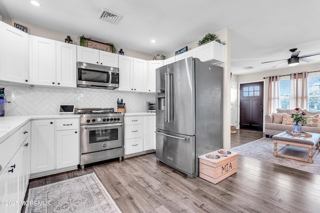 kitchen featuring tasteful backsplash, premium appliances, ceiling fan, light hardwood / wood-style floors, and white cabinets