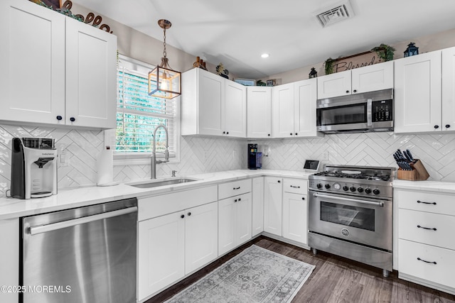 kitchen with appliances with stainless steel finishes, dark hardwood / wood-style floors, white cabinetry, sink, and hanging light fixtures