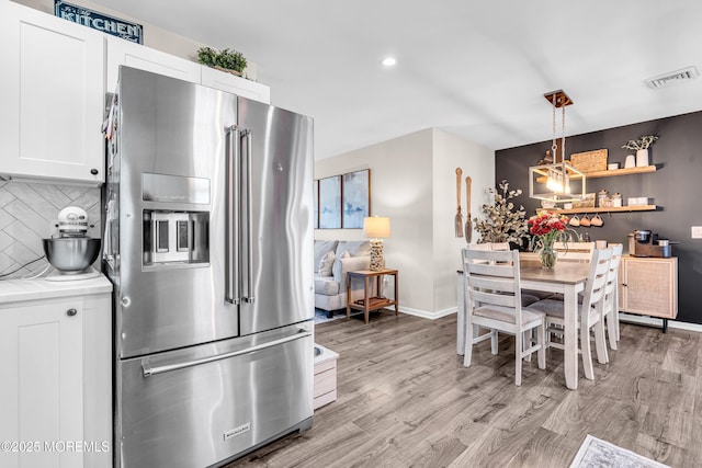 kitchen featuring backsplash, high quality fridge, light hardwood / wood-style floors, white cabinets, and decorative light fixtures