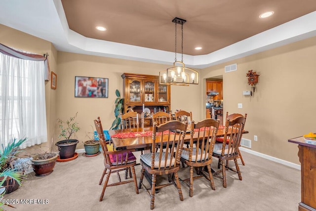 dining room with light carpet, visible vents, a tray ceiling, and baseboards