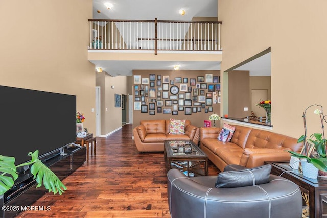 living room with dark wood-type flooring, a towering ceiling, and baseboards