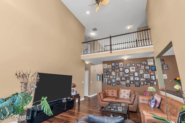 living area featuring visible vents, baseboards, a towering ceiling, ceiling fan, and wood finished floors