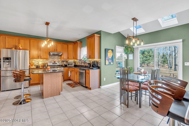 kitchen with under cabinet range hood, stainless steel appliances, a kitchen island, hanging light fixtures, and plenty of natural light