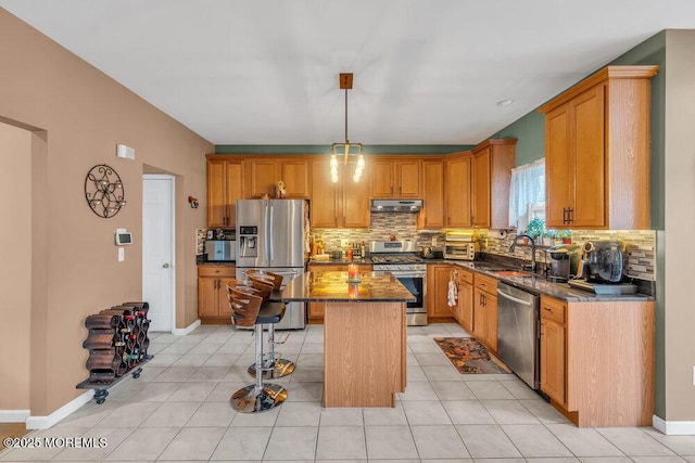 kitchen with decorative light fixtures, stainless steel appliances, a kitchen island, dark stone countertops, and under cabinet range hood