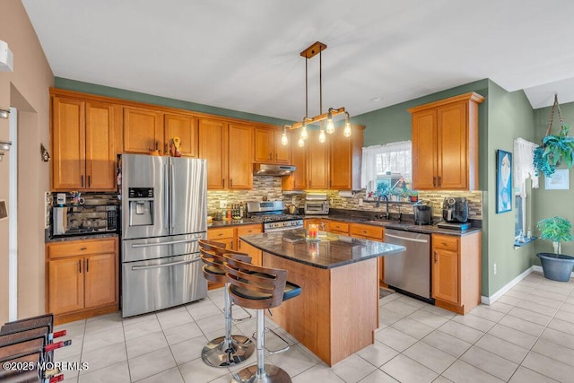 kitchen with under cabinet range hood, stainless steel appliances, a breakfast bar, hanging light fixtures, and a center island