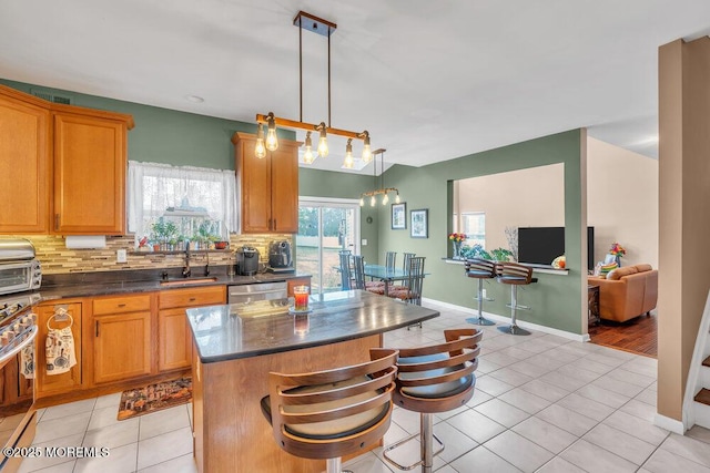 kitchen with decorative backsplash, dark countertops, appliances with stainless steel finishes, a center island, and hanging light fixtures