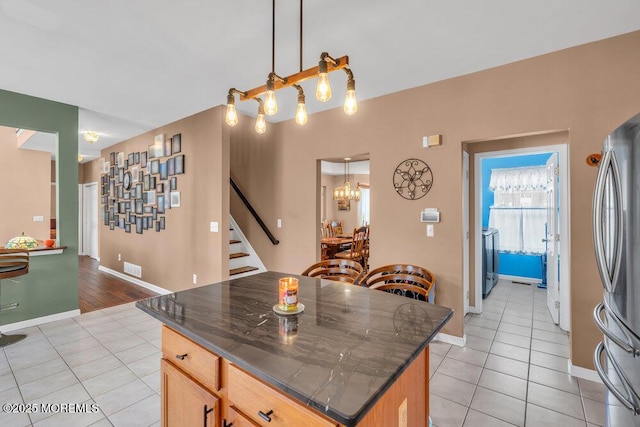 kitchen featuring dark countertops, light tile patterned flooring, decorative light fixtures, and freestanding refrigerator