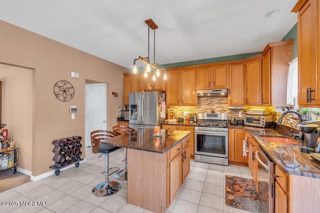 kitchen with light tile patterned floors, under cabinet range hood, a sink, a kitchen island, and appliances with stainless steel finishes