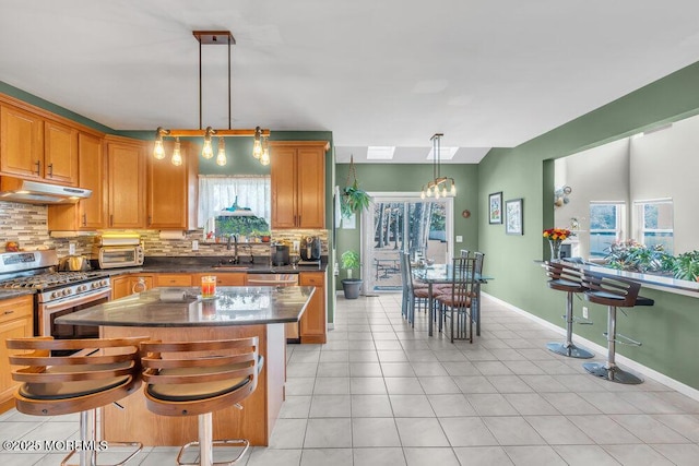 kitchen featuring decorative light fixtures, stainless steel appliances, decorative backsplash, a sink, and under cabinet range hood