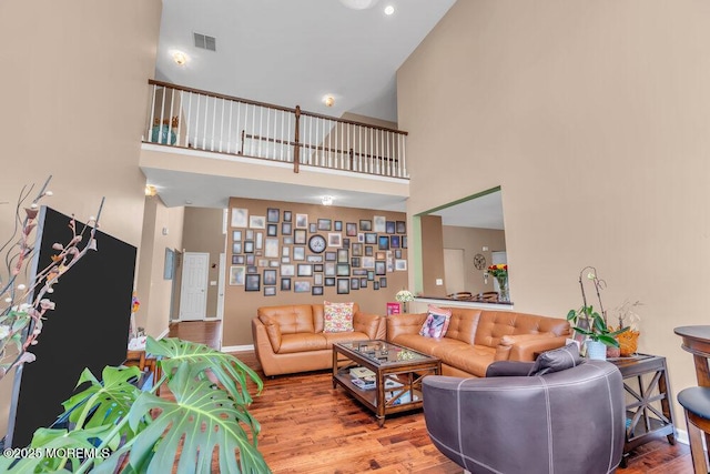 living room with visible vents, a towering ceiling, baseboards, and wood finished floors