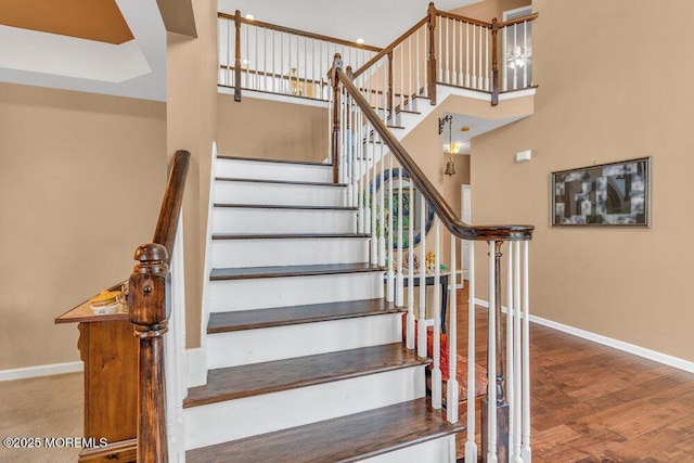 staircase with a towering ceiling, baseboards, and wood finished floors