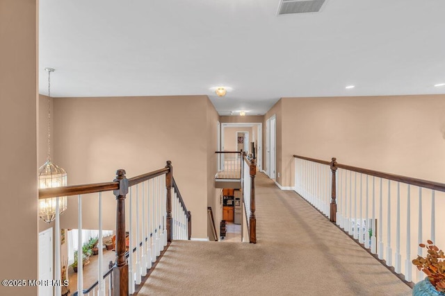 hallway with carpet floors, an upstairs landing, baseboards, visible vents, and an inviting chandelier