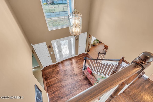 foyer entrance featuring a notable chandelier, wood finished floors, a towering ceiling, baseboards, and stairs