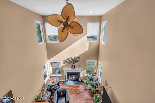 living room featuring ceiling fan, recessed lighting, a high ceiling, wood finished floors, and a fireplace with flush hearth