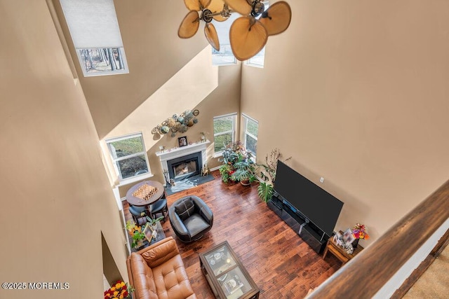 living room with a towering ceiling, a fireplace with flush hearth, ceiling fan, and wood finished floors