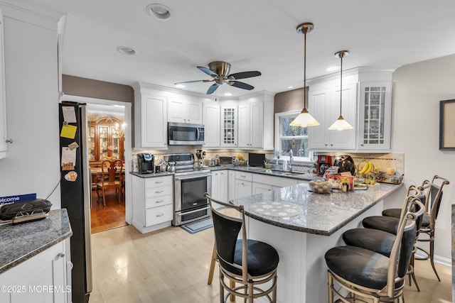 kitchen featuring stainless steel appliances, a kitchen breakfast bar, kitchen peninsula, and hanging light fixtures