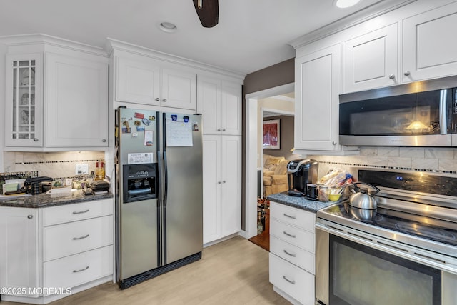 kitchen with white cabinetry, light hardwood / wood-style flooring, dark stone countertops, stainless steel appliances, and backsplash