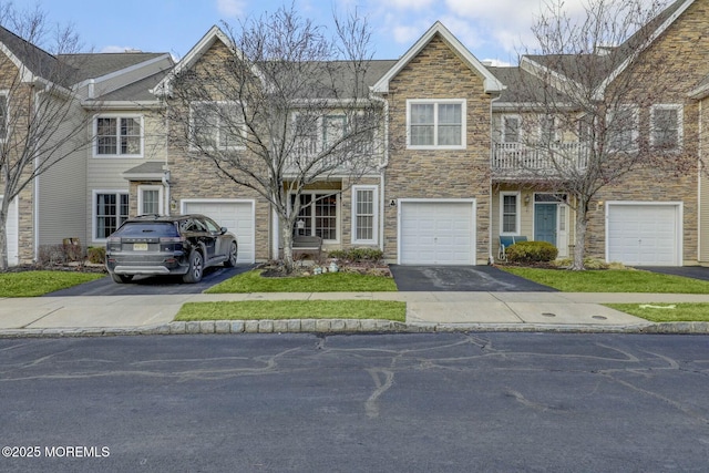 townhome / multi-family property with a garage, stone siding, a balcony, and driveway