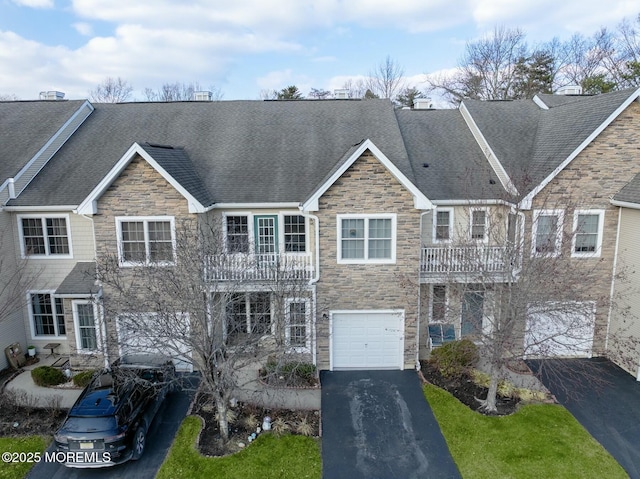 view of property with stone siding, a balcony, driveway, and a garage