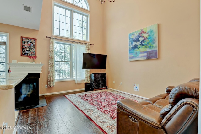 living area with visible vents, dark wood-style floors, a high ceiling, a fireplace, and baseboards