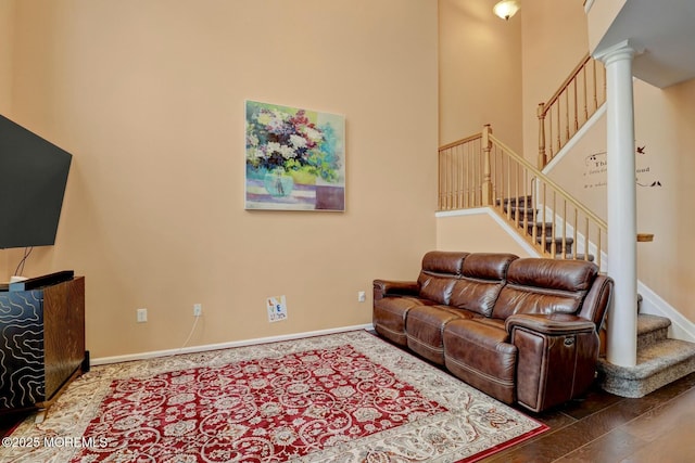 living area with wood finished floors, stairway, a high ceiling, baseboards, and ornate columns