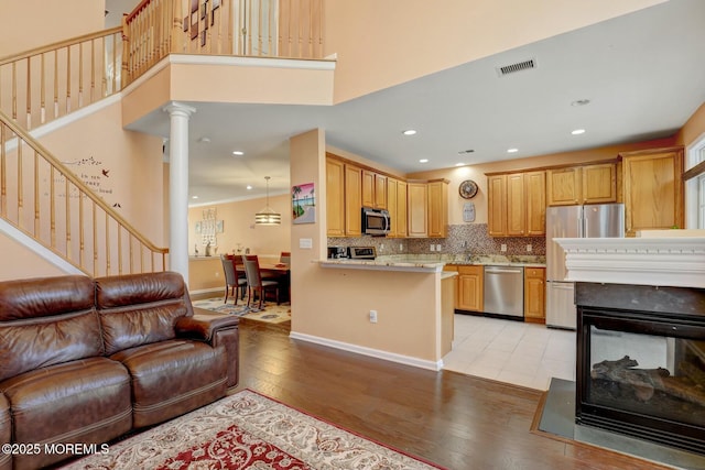 living area with visible vents, stairway, light wood finished floors, decorative columns, and a towering ceiling